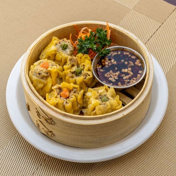 Steamed Thai dumplings, garnished with carrots and parsley, served in a bamboo steamer with dipping sauce.