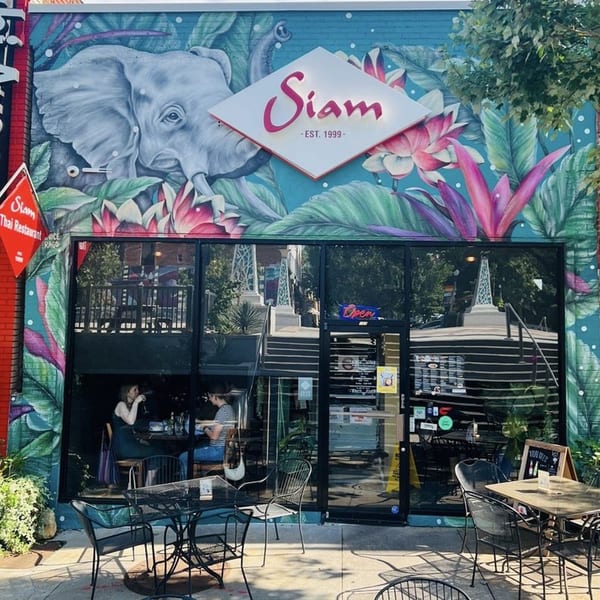 Siam Thai Restaurant exterior with a large elephant mural, outdoor seating, and customers visible inside.