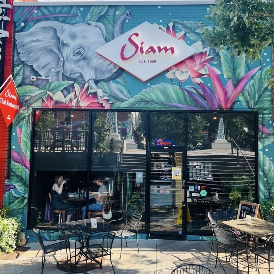 Siam Thai Restaurant exterior with a large elephant mural, outdoor seating, and customers visible inside.